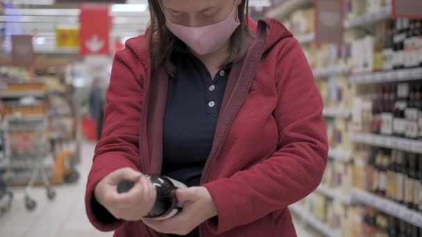 Rosa maskierte Frau steht im Geschäft und hält eine Flasche Rotwein in der Hand — Stockvideo