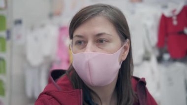 Virüsten pembe maskeli bir kız bebek için kıyafet seçiyor.