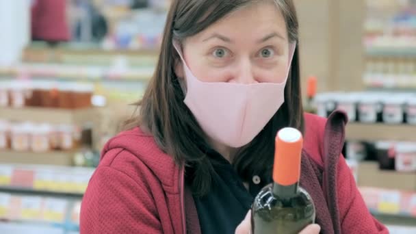 Kobieta w masce medycznej z butelką grimaces wina w sklepie — Wideo stockowe