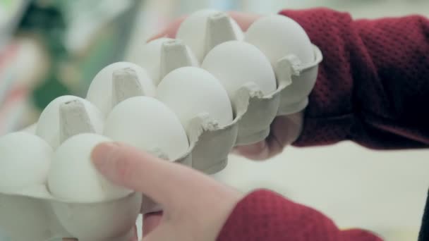 Woman in daub looks package of white, chicken eggs — Stock video