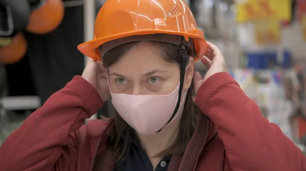 Woman in anti bacterial mask puts on a construction helmet