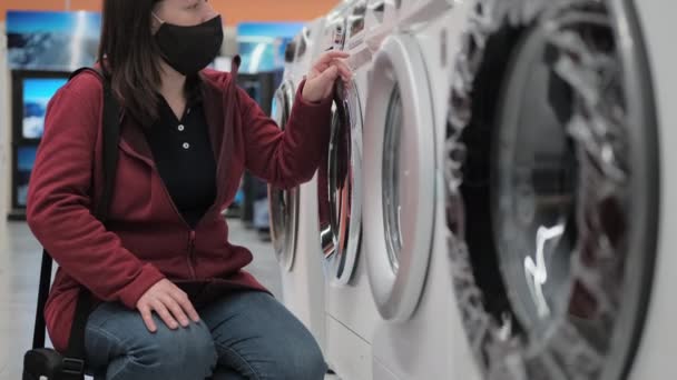 Meisje met een medisch masker koopt een wasmachine in een winkel — Stockvideo