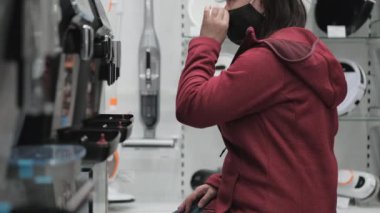 Tıp maskeli kız dükkandan kahve makinesi alıyor.