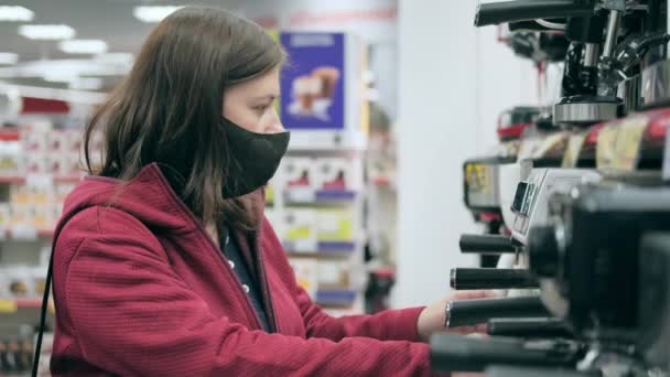 Meisje in zwart medisch masker koopt koffiezetapparaat in de winkel — Stockvideo