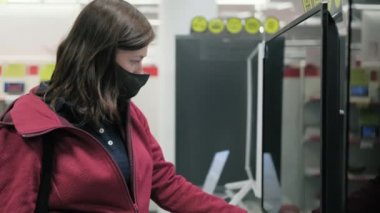 Maskeli kadın elektronik eşya mağazasında yeni bir televizyon seçti
