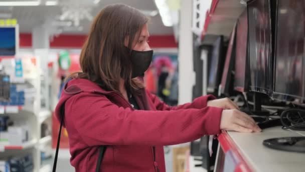 Menina caucasiana na máscara escolhe um novo monitor de desktop na loja — Vídeo de Stock