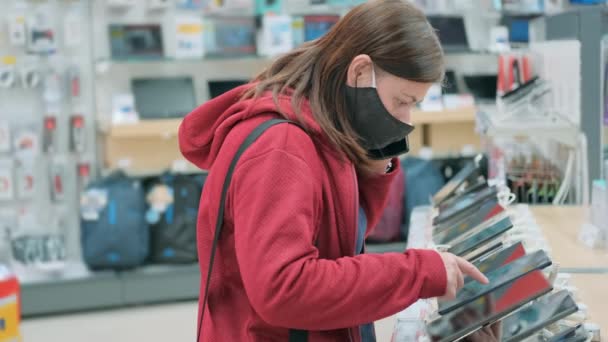 Mädchen mit Maske wählt neues Tablet im Gerätehaus und Gadgets — Stockvideo