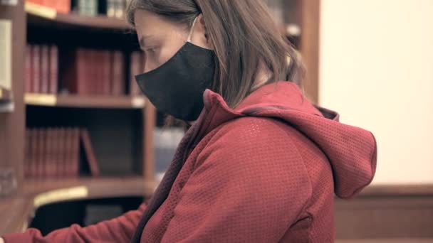 Girl in medical mask quickly flips through a book in library — Stock Video
