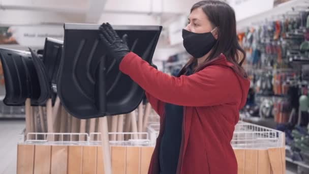 Mulher usando máscara e luvas na loja compra uma pá de neve — Vídeo de Stock