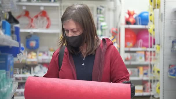 Frau mit Maske und Handschuhen kauft Yogamatte im Geschäft — Stockvideo