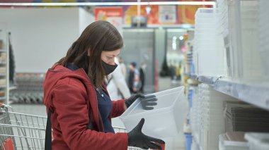Maskeli ve eldivenli kız dükkandan plastik yiyecek kabı alıyor.