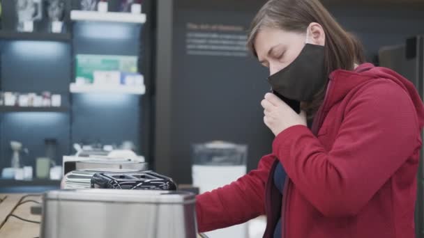 Chica enmascarada escoge una tostadora en una tienda de electrodomésticos — Vídeos de Stock