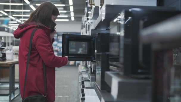 Maszkos lány választ új mikrohullámú sütő elektronikai bolt — Stock videók