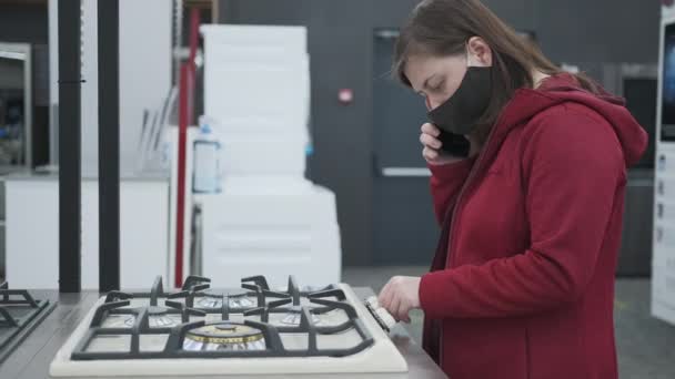 Meisje met een masker koopt een gasfornuis in een winkel voor huishoudelijke apparaten — Stockvideo