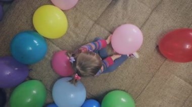 Küçük kız balonlarla oynar, sonra gülümser ve komik bir yüz ifadesi takınır.