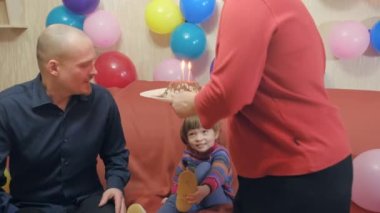 Baba ve anne kızlarını doğum gününde kutluyor, pastadaki mumları üflüyorlar.