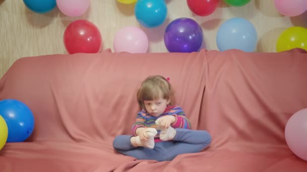 Χαριτωμένο κοριτσάκι που παίζει με τα πόδια της. Υπάρχουν πολλά μπαλόνια τριγύρω. — Αρχείο Βίντεο