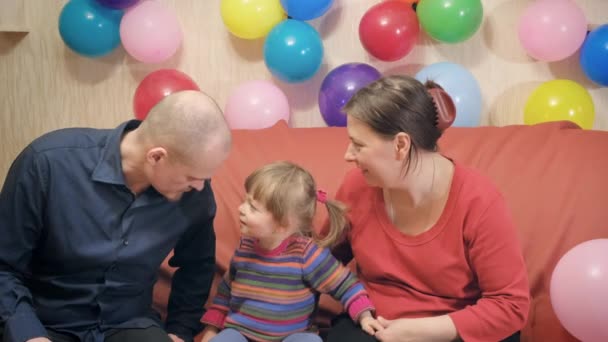 Dad and mom play with their little daughter. There are a lot of balloons around — Stock Video