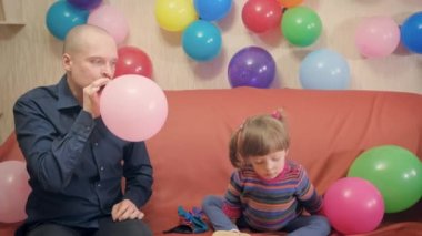 Baba ve kızı pembe bir balon şişirip onunla oynuyorlar.