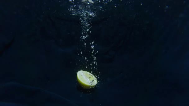 Citron rozříznutý v půli padá do vody ve zpomaleném filmu. Citrusové plody vytvářejí bubliny — Stock video