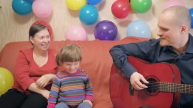 Anne ve baba gitar çalar ve küçük kızlarının doğum günü için şarkı söylerler.
