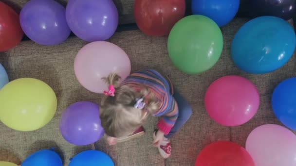 Маленькая забавная девочка играет с разноцветными шариками. Выстрел сверху — стоковое видео