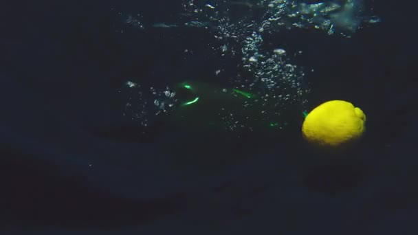 Жовтий лимон плаває у воді, а пластикова пляшка рідини падає зверху — стокове відео