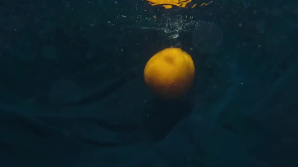 Το πορτοκάλι και το λεμόνι βουτούν αργά κάτω από το νερό. Έννοια της υγιεινής διατροφής — Αρχείο Βίντεο