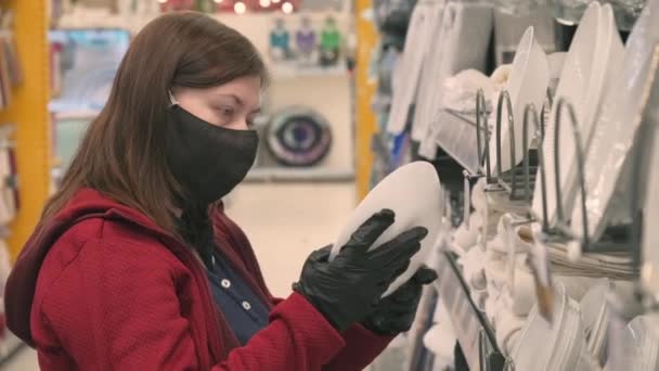 Жінка в масці і рукавички проти вірусу купує білу тарілку в магазині — стокове відео