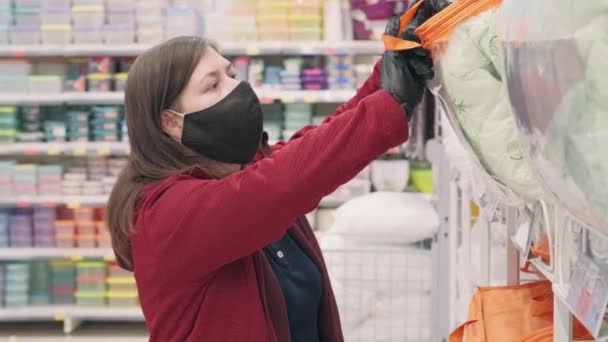 Virüse karşı maske ve eldiven takan bir kız sıcak battaniyeyi mağazadan seçiyor. — Stok video