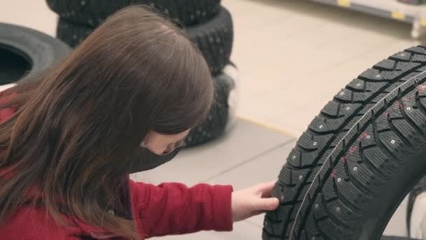 Chica en máscara contra el virus compra neumáticos tachonados para el coche en la tienda. Primer plano. — Vídeos de Stock