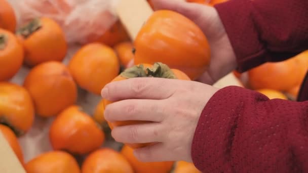 Girl hands in the shop buys a ripe persimmon. Close up shot — Stock Video