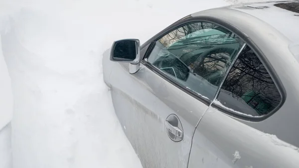 Passenger car, its hood buried in snow. Car door is also blocked snowdrift