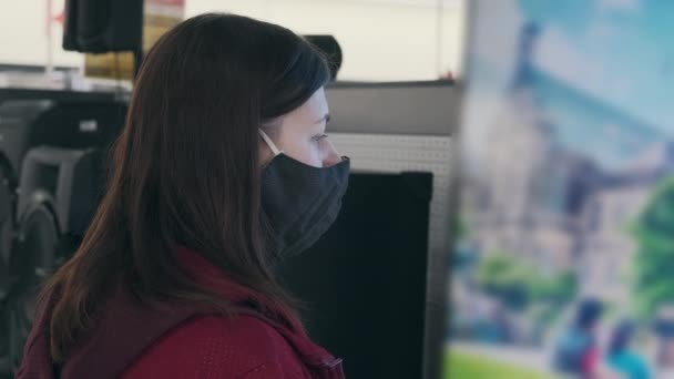 Kvinde i maske og ser skærm af enorme TV i butikken. TV-skærmen er i stærk sløring – Stock-video