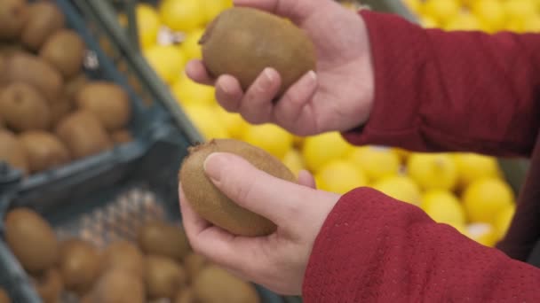 Las manos de la muchacha en la tienda compra una fruta fresca y madura kiwi. Primer plano. — Vídeo de stock