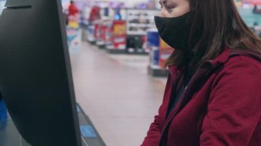 Virüse karşı maske takan ve eldiven takan bir kız, mağaza cihazlarında çukur monitörü satın alıyor