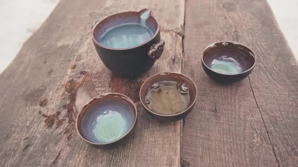 Man hand pours green Chinese tea into clay cups which stand on mahogany planks — Stock Video