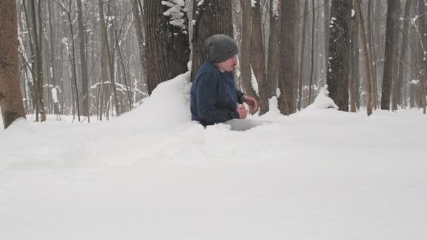 Opilý muž bez bundy zamrzá v lese, sedí na sněhu u stromu — Stock video