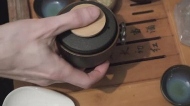 Çay tahtası, kamera yakın çekim. İnsan eli kil bardaklara yeşil oolong döker.
