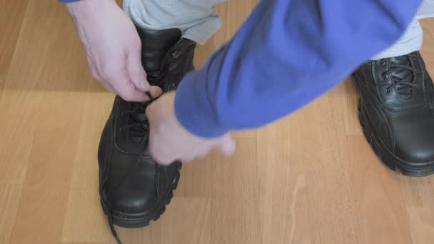 Man in witte broek bindt de veters aan zijn zwarte warme laarzen voor de koude winter — Stockvideo