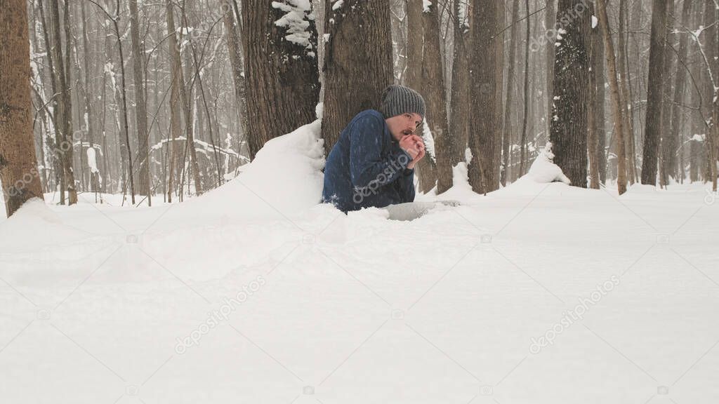 Man without a jacket freezes in the forest sitting on snow near a tree