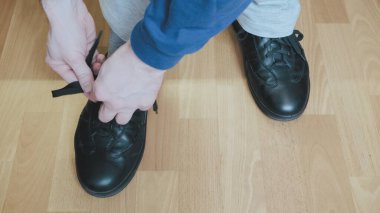 Mavi ceketli ve beyaz pantolonlu adam siyah ayakkabıların bağcıklarında bir fiyonk yapıyor.
