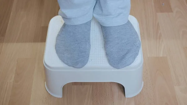 Men feet in white pants and gray socks stand on a plastic stool. Close up shot