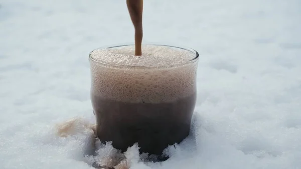 浓烈的黑啤酒倒入雪地里的杯子里 — 图库照片