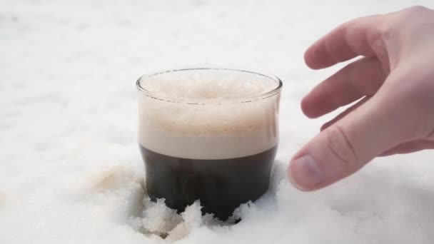Uomo mano raccoglie un bicchiere di freddo, scuro, forte birra robusta dalla neve — Video Stock