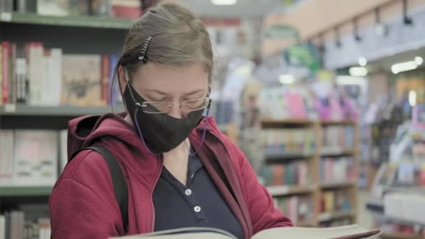 Een vrouw met een masker leest een boek. Ze knipt met haar ogen en doet zijn bril af. — Stockvideo