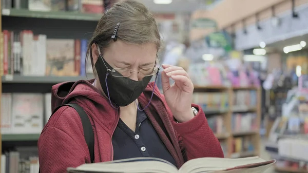 Woman in mask reads book. She squints eyes. Concept of migraine and headache