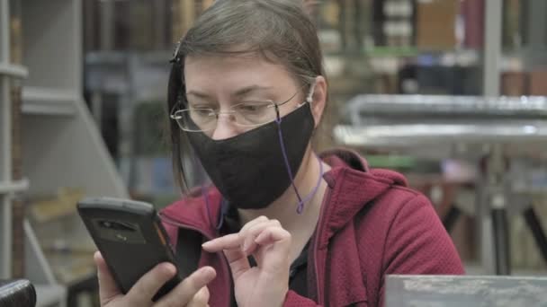 Vrouw met bril en masker in de boekhandel neemt foto 's van boeken op haar telefoon — Stockvideo