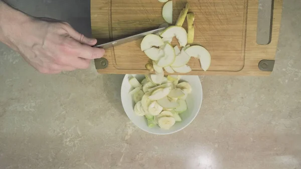 Man skär päron och lägger det med äpplen och banan för att göra en söt, fruktsallad — Stockfoto