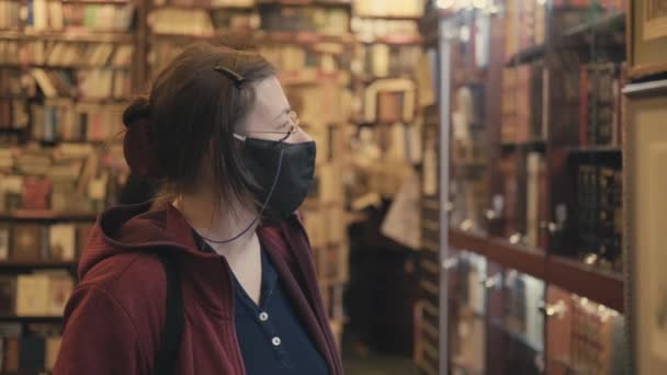 Woman in glasses and mask against virus chooses painting to buy in antique shop — Stock Video